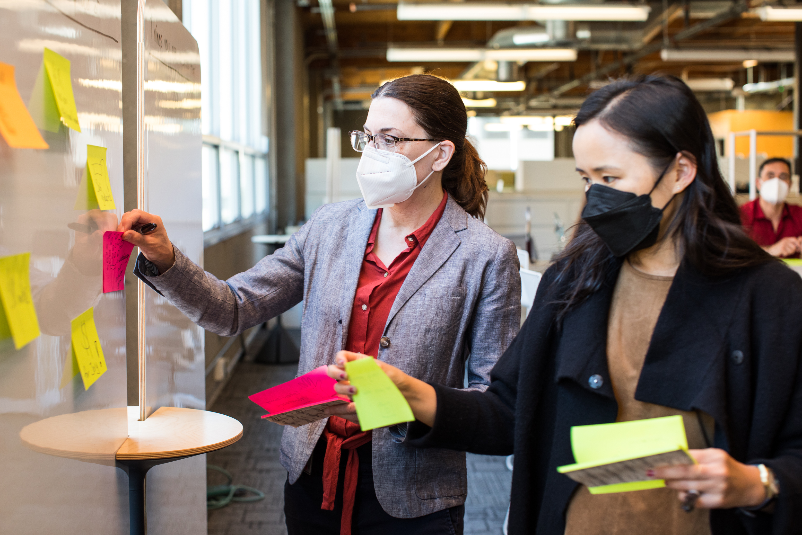 Two people wearing masks stand in front of a white board and apply sticky notes.